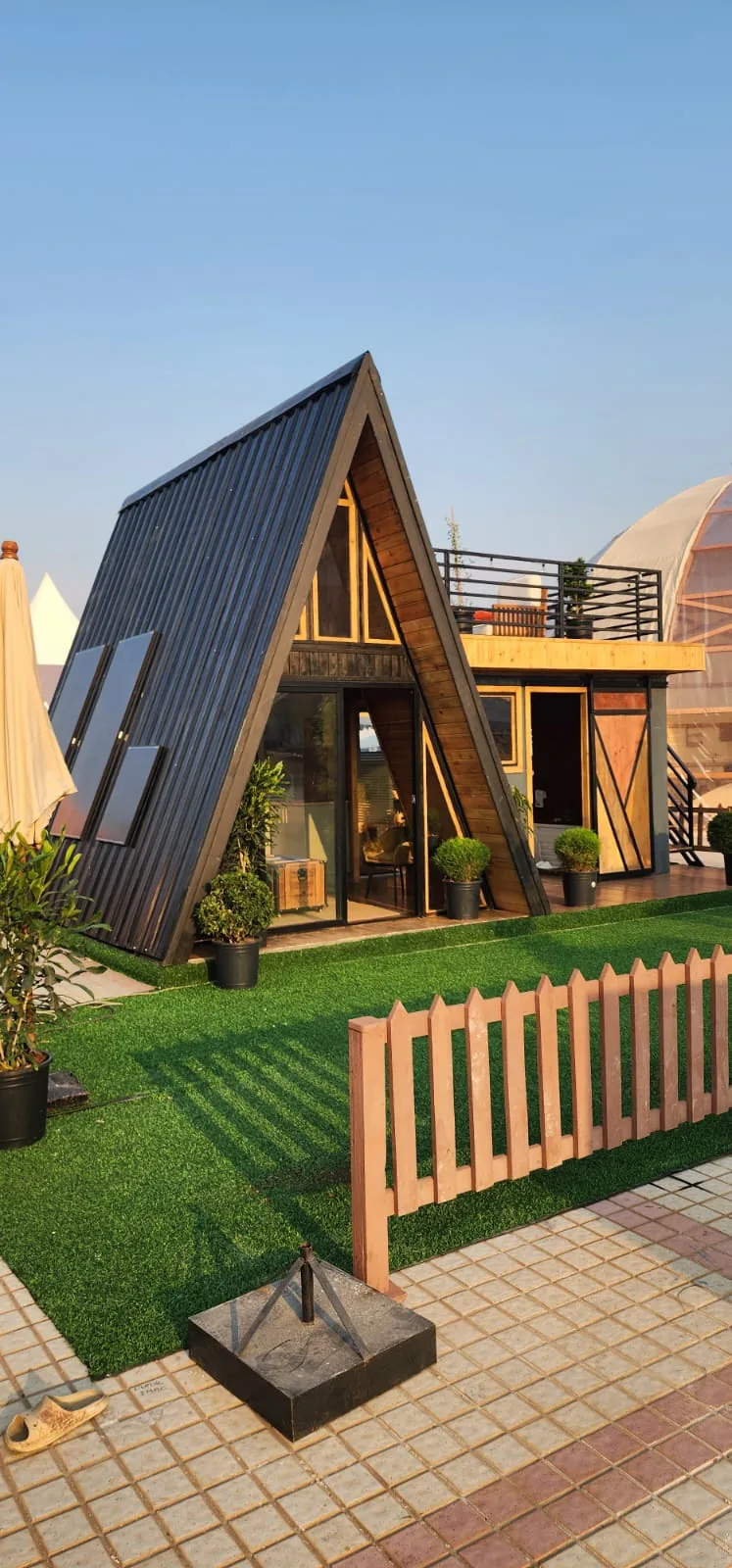 Maison A-Frame vue de trois quarts, toit en bac noir, pignon bois et baie vitrée