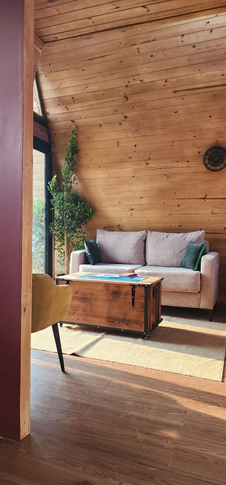Salon de la maison A-Frame : canapé, malle table basse bois et métal, murs en lambris